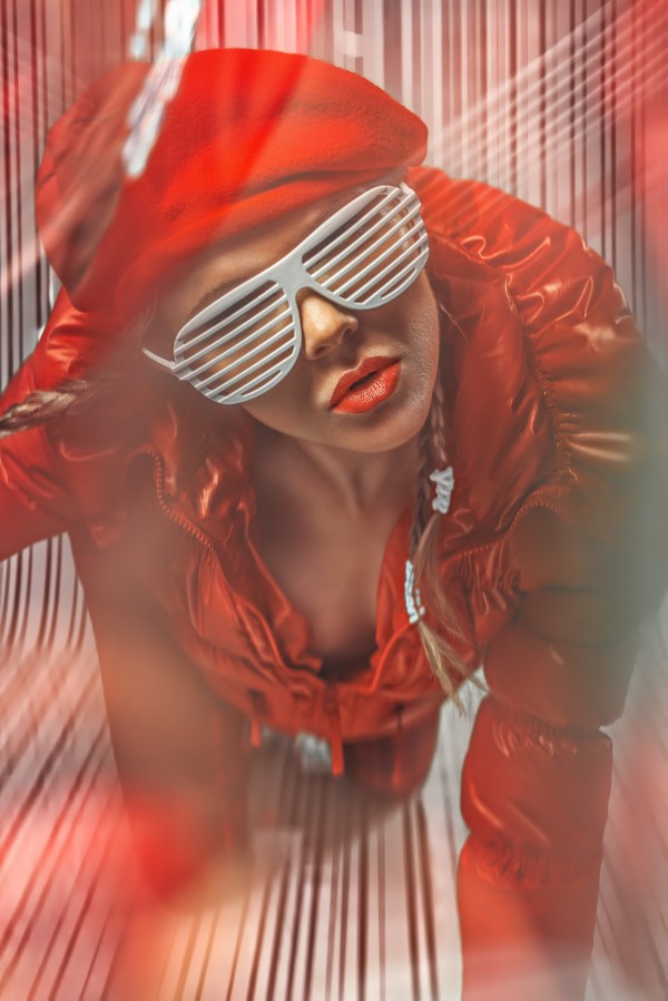Beautiful blonde fashion model wearing braids in a red outfit with grill glasses posing in a white striped plastic environment by Artmood Visualz